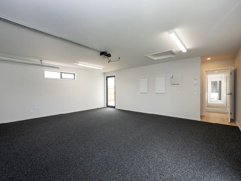 Carpeted double garage in the Heart Foundation Home Lottery 162 three-bedroom house in Richmond, Nelson with internal hallway access and external door.