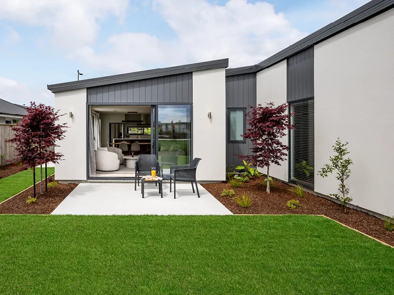 Landscaped backyard and patio of the Heart Foundation Home Lottery 162 three-bedroom house in Richmond, Nelson with outdoor seating and sliding doors to living area.