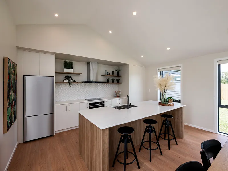Modern Whitianga kitchen with vaulted ceiling, white cabinetry, wood island bench with breakfast bar stools, stainless steel appliances and open shelving styled with plants and decor.