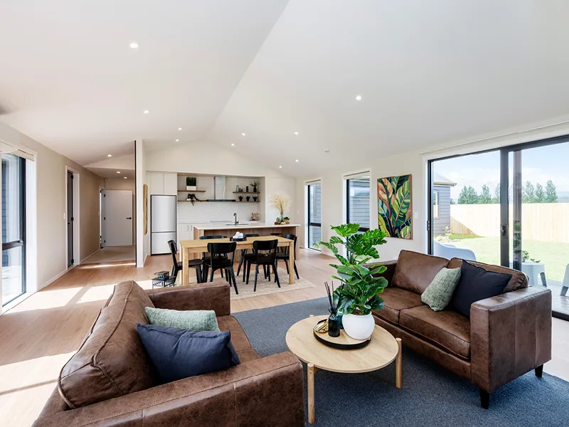 Modern Whitianga open-plan living area with brown leather sofas, round coffee table and indoor plants, flowing to contemporary kitchen and dining space with large sliding doors to the backyard.
