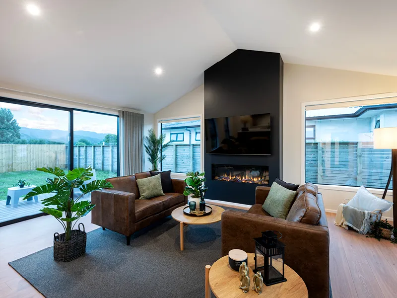 Modern Whitianga living room with brown leather sofas, gas fireplace feature wall with mounted TV, large sliding doors to deck and landscaped backyard, styled with indoor plants and neutral decor.