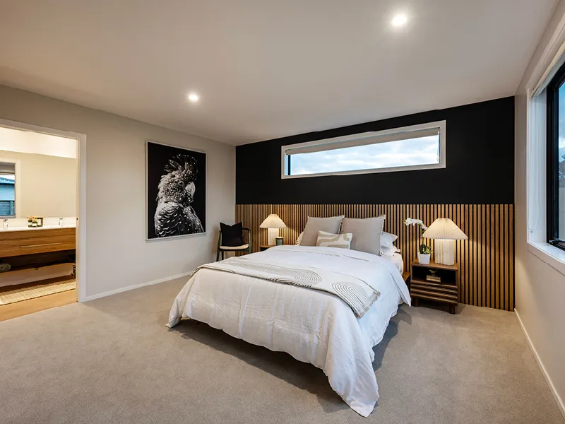 Modern Whitianga master bedroom with timber slat feature wall and horizontal window, styled with neutral bedding, matching bedside tables and lamps, and ensuite visible through open doorway.