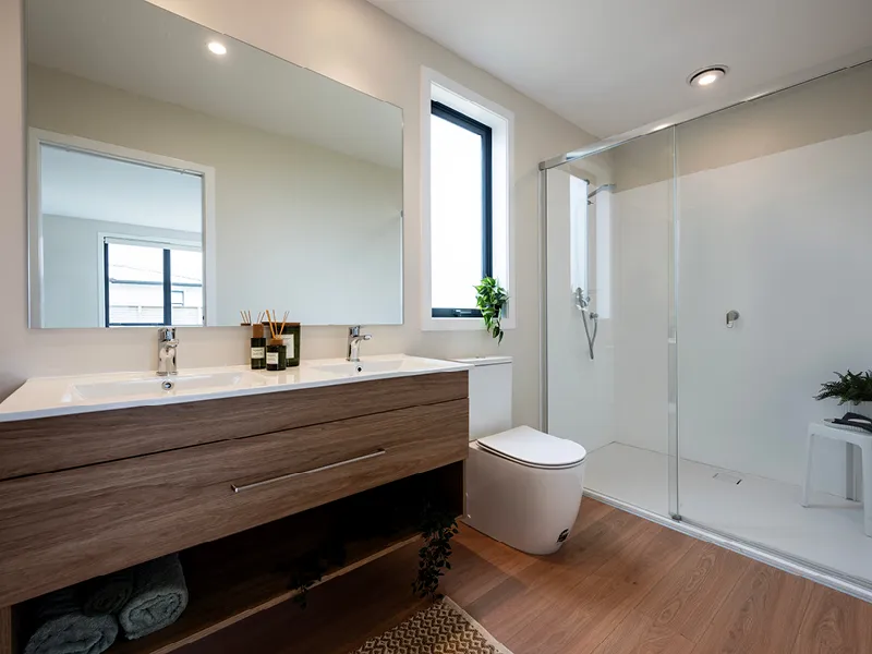 Modern Whitianga bathroom with double vanity and large mirror, walk-in glass shower, timber-look flooring and minimalist decor with black-framed window and greenery accents.