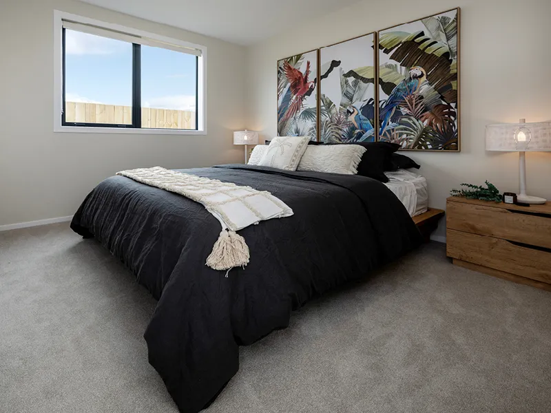 Modern Whitianga bedroom with black bedding, timber bedside tables and tropical parrot artwork triptych above the bed, styled with neutral tones and large window for natural light.