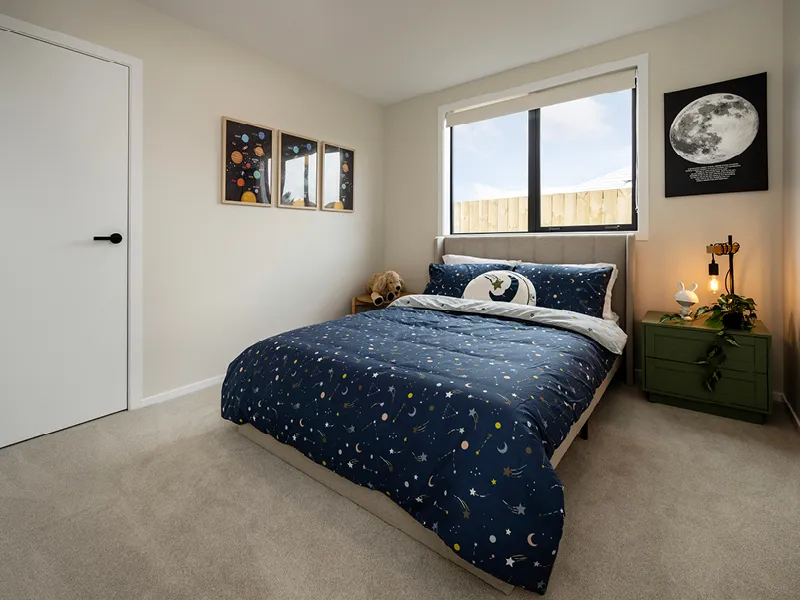 Modern Whitianga kids’ bedroom with space-themed navy bedding, solar system wall art and moon print, styled with green bedside table and large window for natural light.
