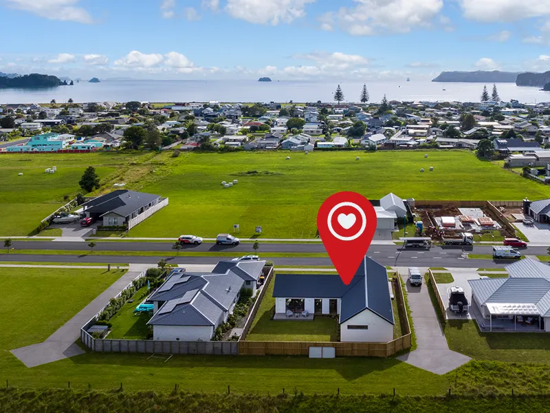 Aerial view of Whitianga coastal suburb showing modern Lottery 163 home highlighted with location pin, set on fenced section close to reserve and beach.