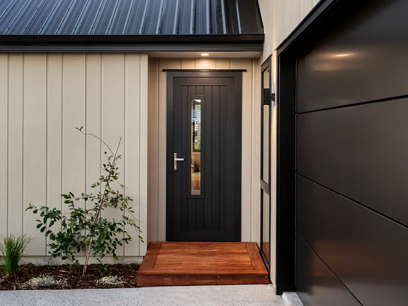 Modern Kinloch home entrance with dark feature front door, timber step, vertical cladding and low‑maintenance landscaping.