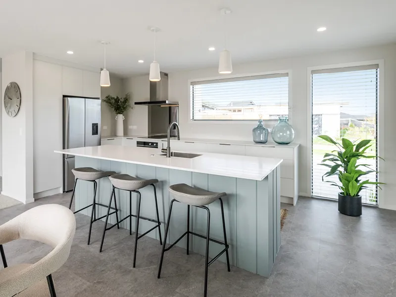 Modern Kinloch open‑plan kitchen with white island bench, stainless steel appliances and styled living area in background.