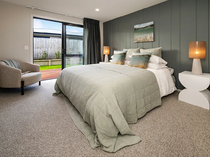 Kinloch master bedroom with panelled feature wall, large bed, bedside lamps and sliding doors to outdoor deck.