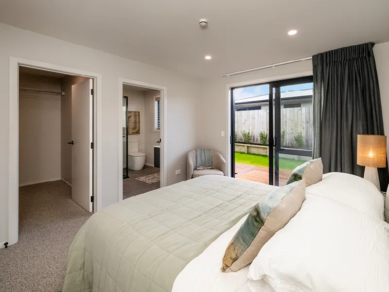 Kinloch master bedroom showing walk‑in wardrobe, ensuite bathroom and access to private deck and lawn.