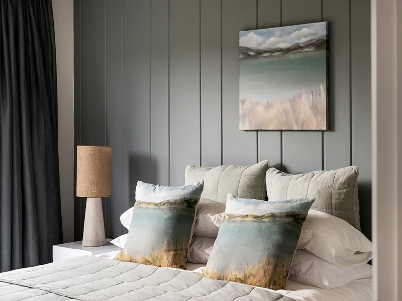 Stylish Kinloch bedroom feature wall with landscape artwork, textured cushions and bedside lamp.