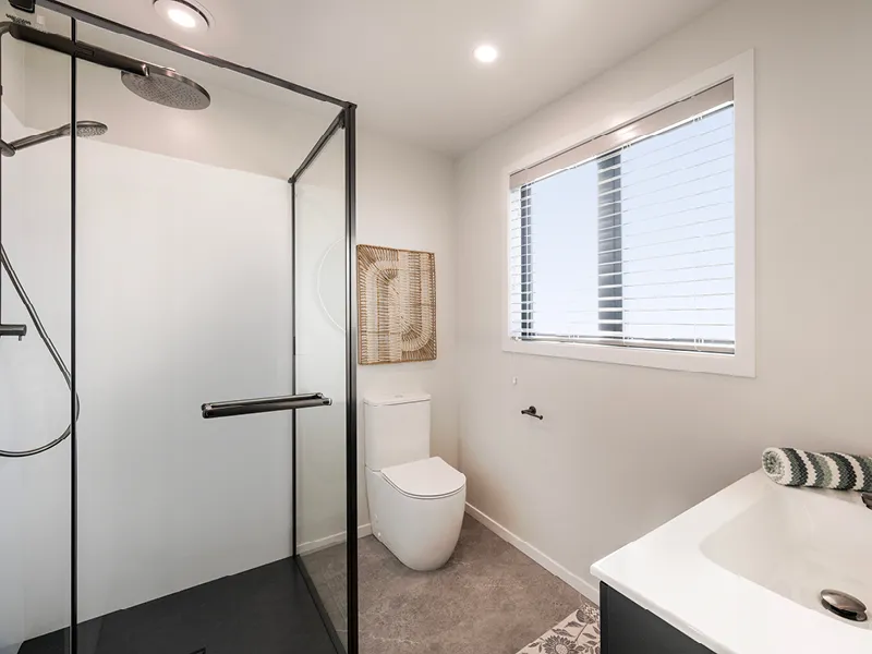 Modern Kinloch bathroom with black‑framed glass shower, toilet, vanity and large window providing natural light.