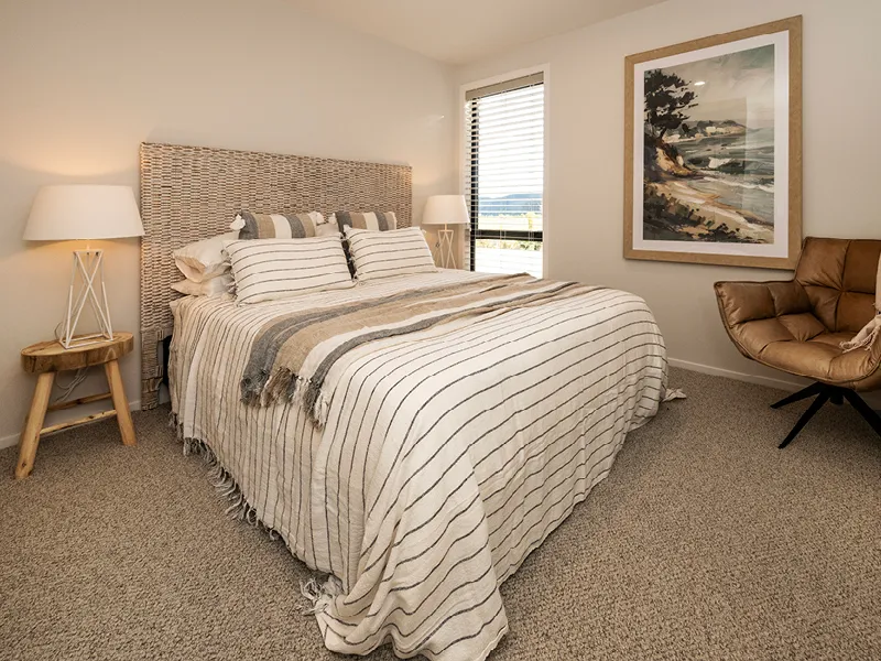 Guest bedroom in Kinloch home with striped bedding, woven headboard, coastal artwork and accent chair.