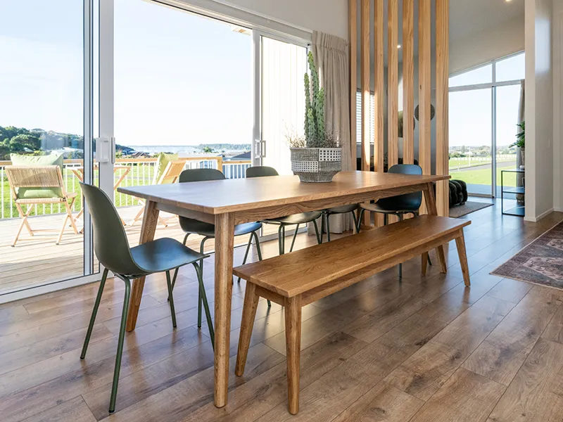 Dining area with timber table and bench seating opening onto a deck with coastal views in the Heart Foundation Home Lottery No. 165 house.