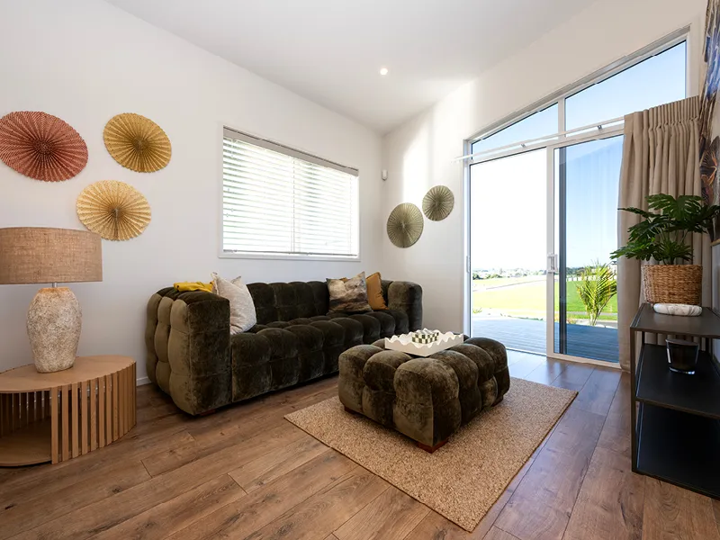 Cosy sitting room with olive velvet sofa, ottoman and paper fan wall art overlooking rural views in the Heart Foundation Home Lottery No. 165 Ōmokoroa house.