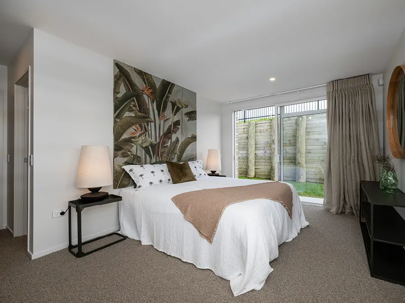 Main bedroom with king bed, botanical wall art and sliding door to a fenced courtyard in the Heart Foundation Home Lottery No. 165 Ōmokoroa house.