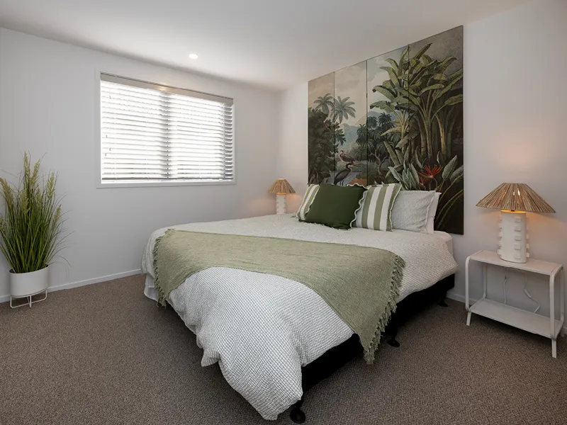 Second bedroom with king bed, tropical palm-print wall art and white timber blinds in the Heart Foundation Home Lottery No. 165 Ōmokoroa house.