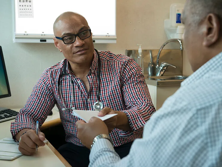 A doctor and patient meet in the clinic. the doctor passes his patient a prescription.