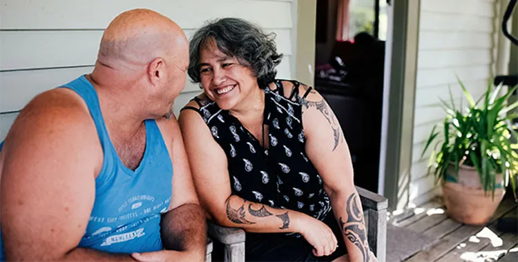 Middle-aged Maori couple sitting on their deck looking at each other and smiling