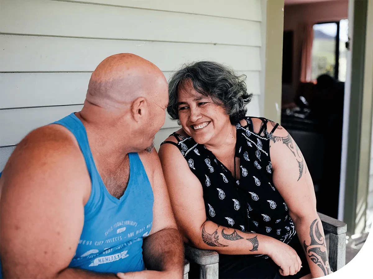 Older Maori couple sitting on their deck and looking lovingly into each other'seyes.