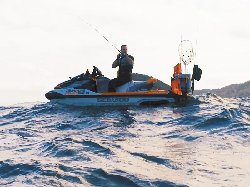 Adventure fisherman, Andrew Hill, is pictured here sitting on top of his jet ski in the middle of the ocean. He is fishing from the jet ski and the photo captures him mid-cast off.