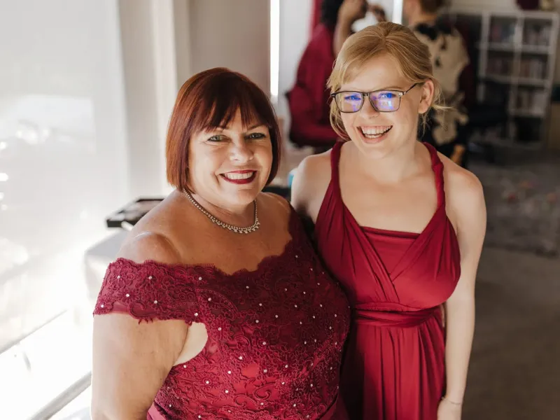 Hannah smiling alongside another woman, both wearing burgundy dresses.