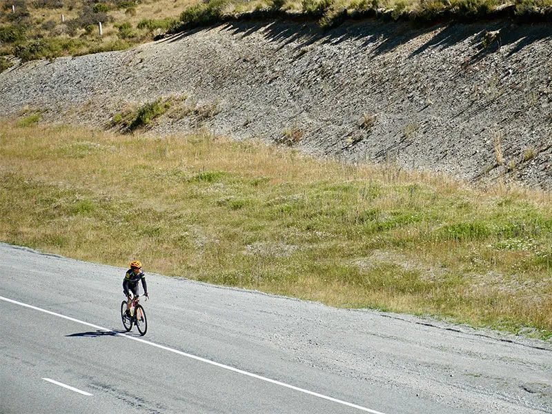 Kara Northcott appears as a tiny figure on a bike in a hilly landscape. She is wearing full cycling gear.
