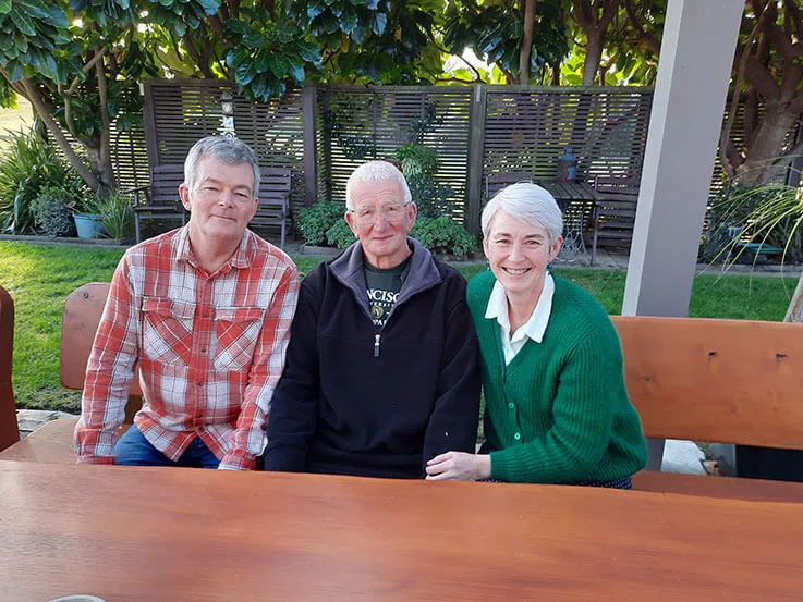 Family photo of Stuart Jones, his daughter Tonya and his son-in-law Lance, sitting on a bench in their garden.
