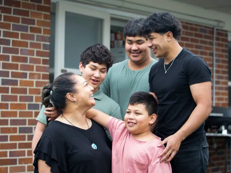 Family standing together outside brick home, representing whānau support for rheumatic heart disease care and heart health in New Zealand