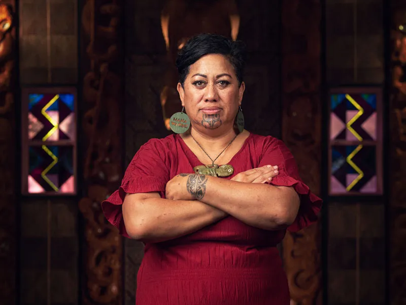 This image depicts Mereana Hona (Maori woman) standing in front of a Po. She stands with her arms folded across her chest.