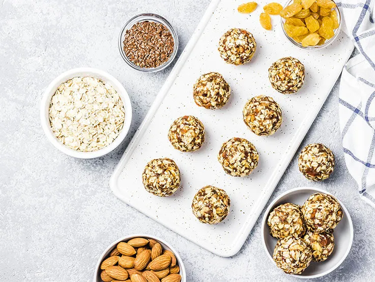 Raw vegan healthy dessert, date and nuts bliss balls, with the ingredients set alongside in small white ceramic bowls. 