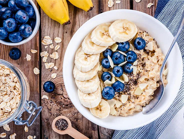 Porridge in a white bowl with bananas, blueberries and chia seeds on top. 