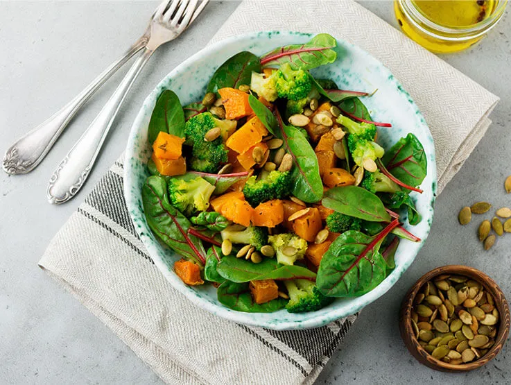 Salad with a baked pumpkin, kale, broccoli, and pumpkin seeds in ceramic plate on stone or concrete background table background. Rustic style.
