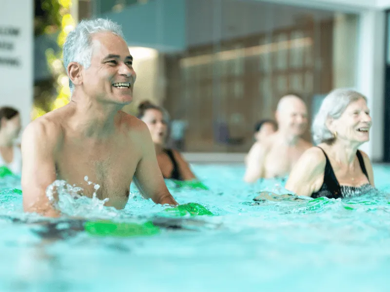 Older adults taking part in aqua aerobics class, doing water based exercise for heart health and low impact fitness in a swimming pool.