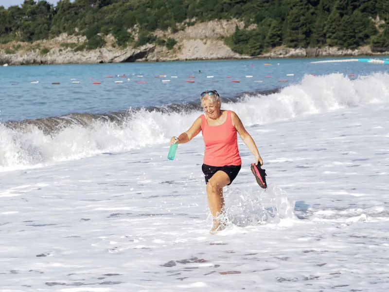 Woman walking through shallow sea water on sandy beach, doing gentle water based exercise for heart health and fitness.