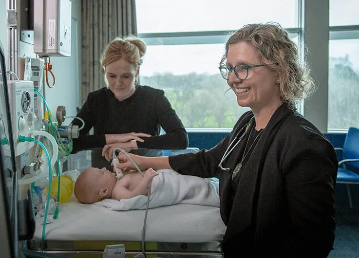 Dr Sarah Harris performs a heart ultrasound on a newborn infant, with the baby's mother looking on.