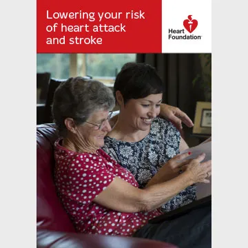 A senior woman and her middle-aged daughter sit together on a sofa, looking through the 'Lowering your risk of heart attack and stroke' booklet.
